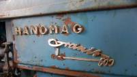 Auf einer mit alten angerosteten, dunkelblauen Traktor-Karosserie steht in beschlagenen Lettern &#039;Hanomag&#039;